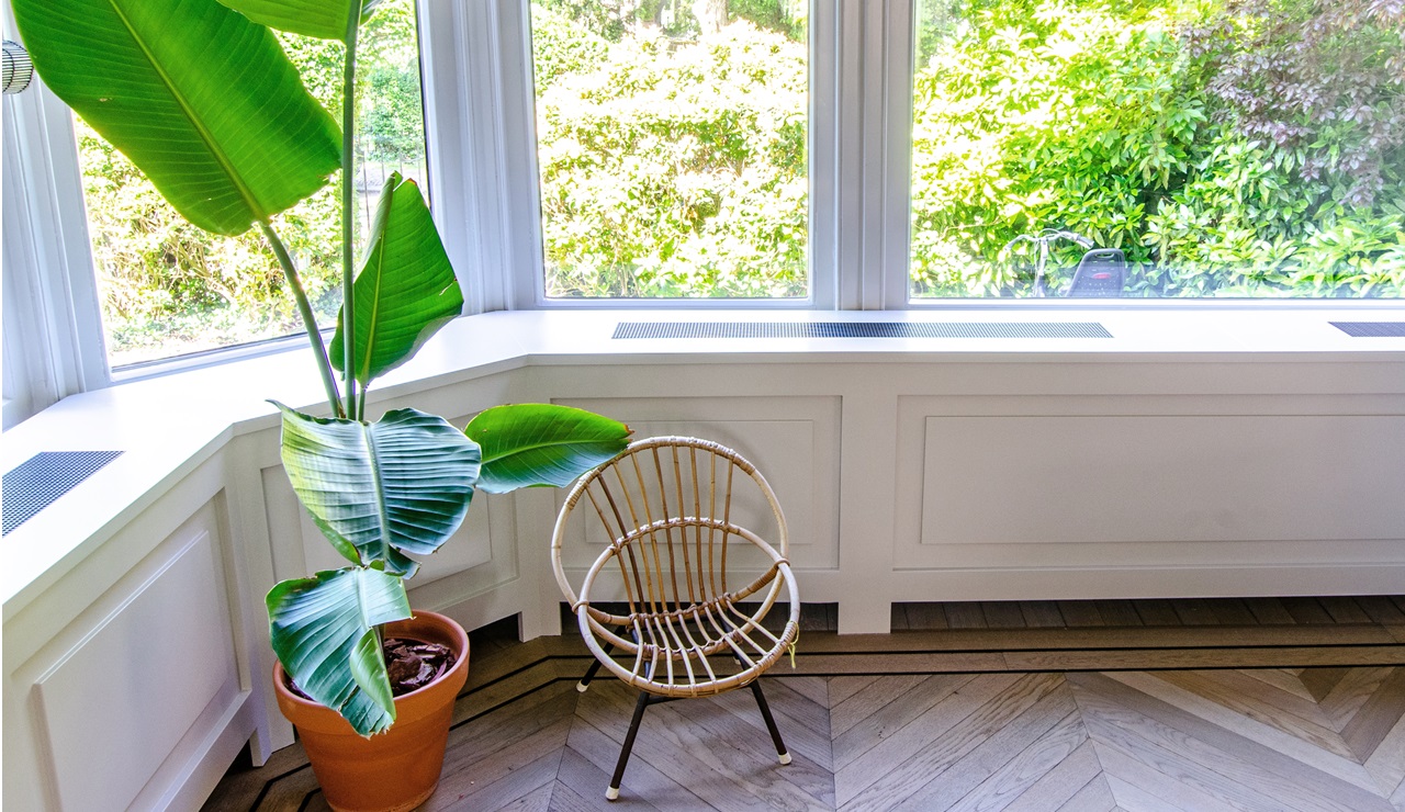 De Wandinbouw Hybrid LT-convector is hier weggewerkt achter een houten omkasting. Onder is ruimte vrijgehouden, wat nodig is voor de aanvoer van lucht die er aan de bovenkant via de roosters weer uitkomt.