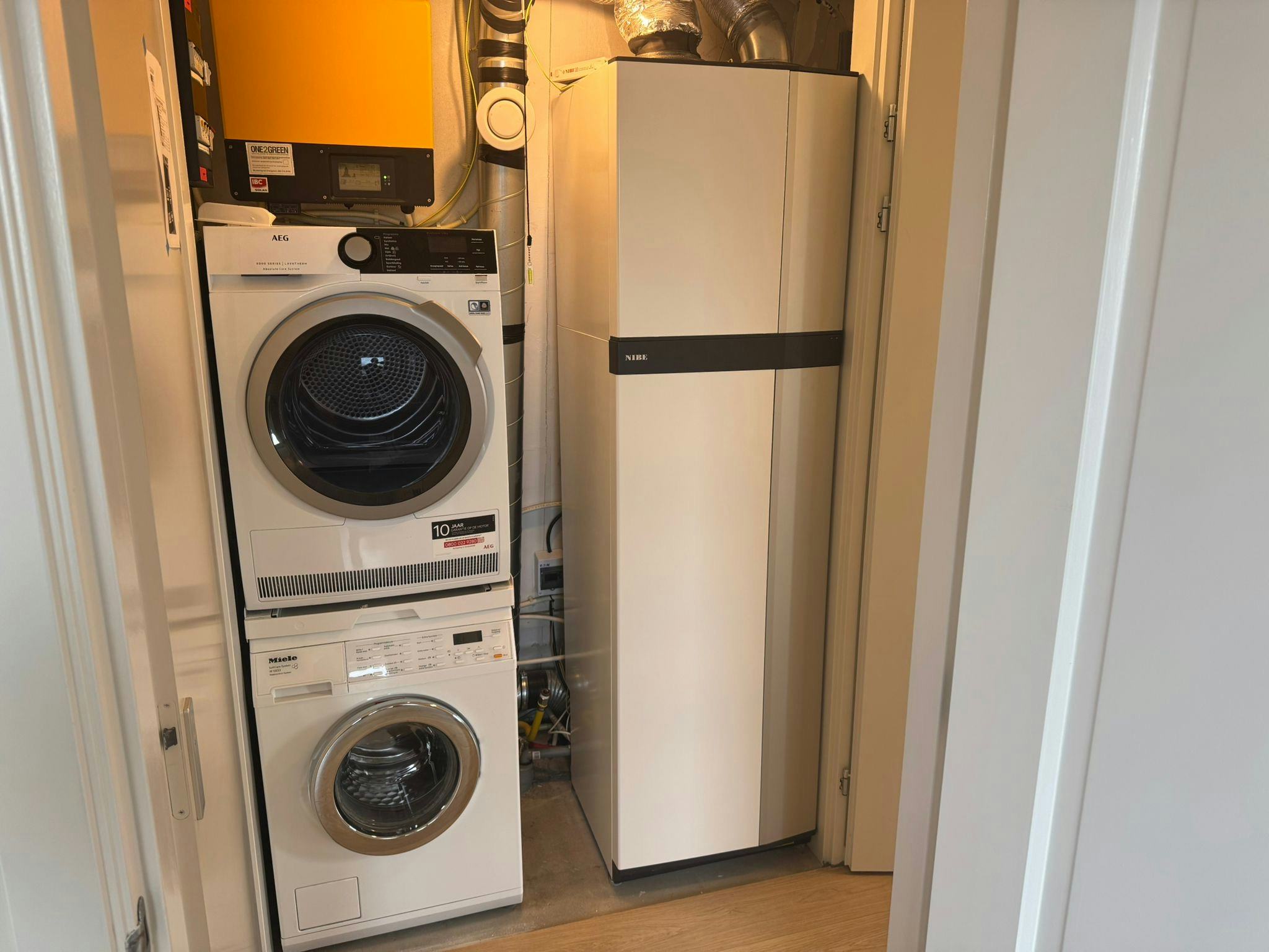 De ventilatiewarmtepomp met boilervat naast de wasmachine en -droger.